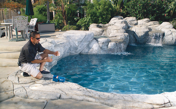 The Pool Guy kneeling at a pool, testing the water with a test kit
